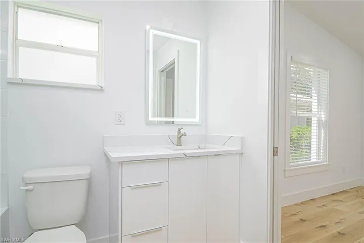 Bathroom with toilet, vanity, wood finished floors, and baseboards