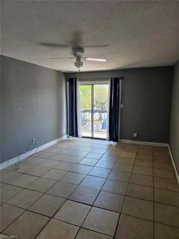 Spacious room featuring neutral tile flooring, a ceiling fan, and sliding glass doors opening to an exterior area