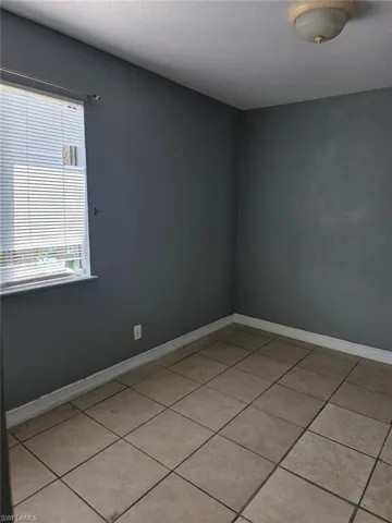 Interior room featuring neutral-toned tile flooring, dark gray walls, and white baseboards