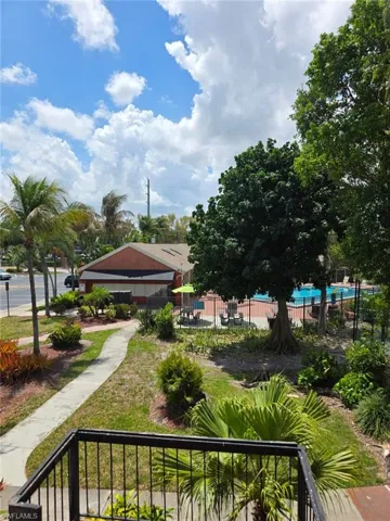 Outdoor common area featuring a curved pathway, mature trees, and a fenced swimming pool with surrounding patio seating