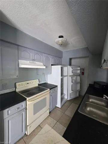 Kitchen featuring grey cabinetry, dark countertops, a white electric range, and a double basin stainless steel sink