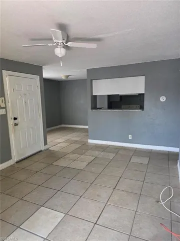Living space featuring tile flooring, a ceiling fan with integrated lighting, and a pass-through window with a countertop into an adjacent room