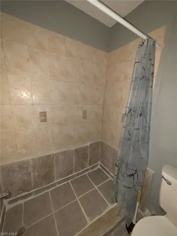 Shower enclosure featuring light-toned wall tiling, contrasting darker floor tiles, and a white shower rod