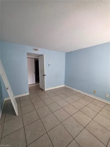 Spacious interior room featuring tile flooring, light blue walls, white trim, and a white ceiling with a visible vent