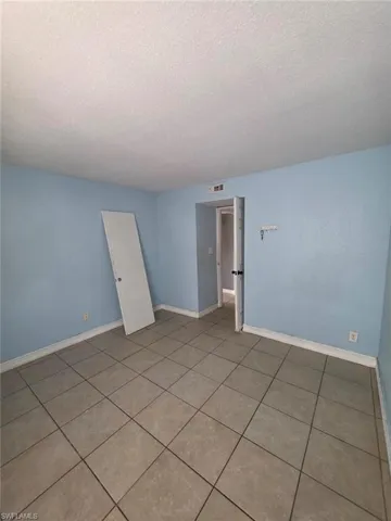 Spacious room with light blue walls, neutral-toned square tile flooring, white baseboards, and a white ceiling