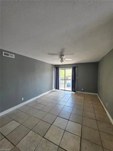 Spacious room featuring tile flooring, a ceiling fan with integrated lighting, and a sliding glass door