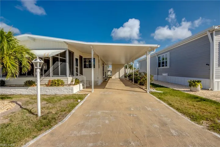View of front of property with concrete driveway, a front lawn, and a carport