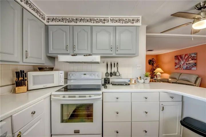 Kitchen with decorative backsplash, a ceiling fan, range hood, light countertops, and white appliances