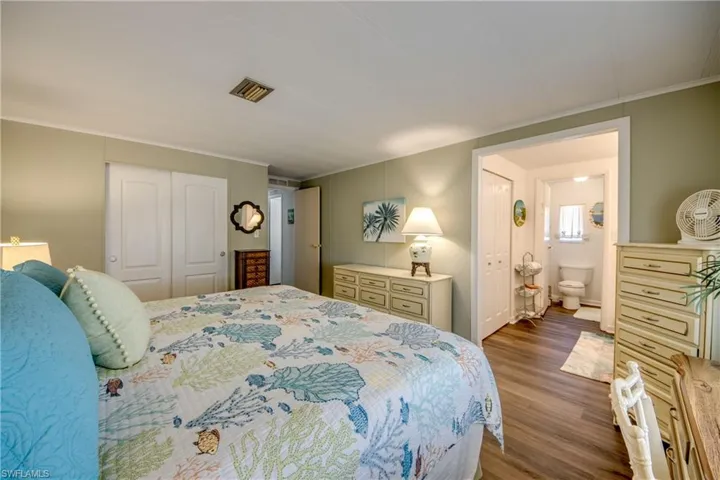 Bedroom with visible vents, wood finished floors, a closet, connected bathroom, and ornamental molding