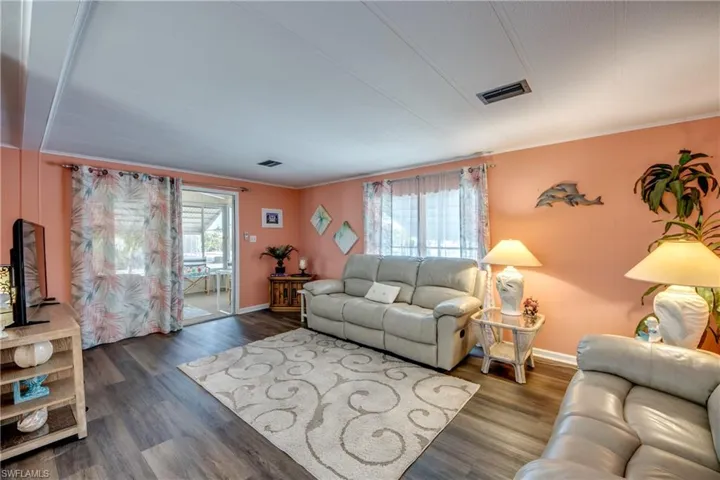 Living area with crown molding, baseboards, wood finished floors, and visible vents