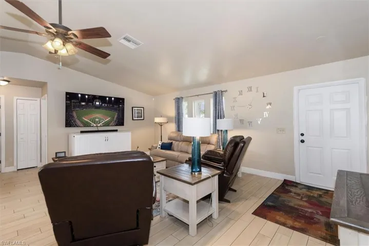 Living room featuring a ceiling fan, light wood-style floors, vaulted ceiling, baseboards, and radiator