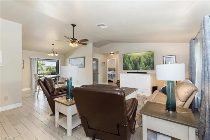 Living area with a ceiling fan, lofted ceiling, baseboards, a chandelier, and light wood-type flooring