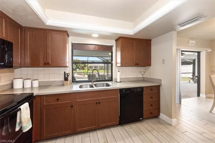 Kitchen with black appliances, a sink, tasteful backsplash, and a raised ceiling