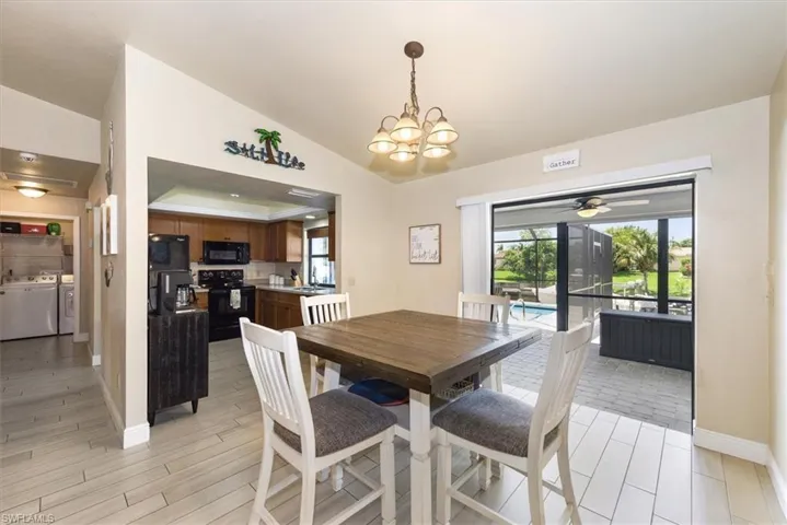 Dining area with washing machine and dryer, vaulted ceiling, light wood-style floors, baseboards, and a chandelier