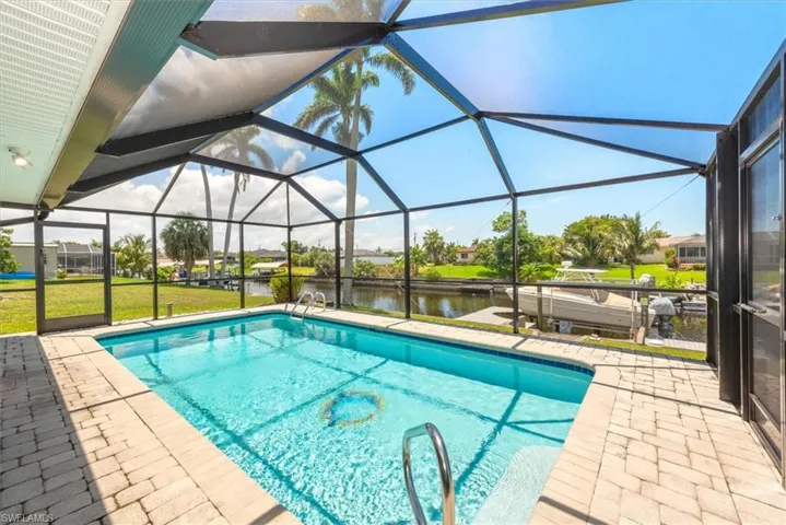 Outdoor pool featuring a patio, a water view, and glass enclosure