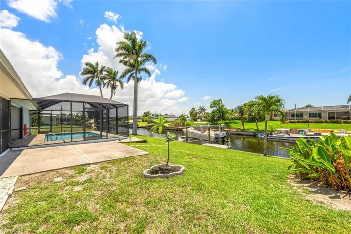 View of grassy yard with a water view, a patio area, an outdoor pool, glass enclosure, and a boat dock