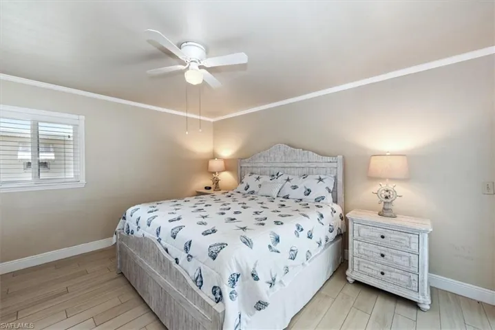 Bedroom featuring light wood-type flooring, baseboards, ornamental molding, and a ceiling fan