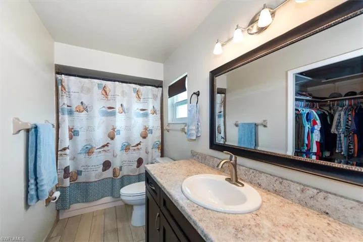 Bathroom featuring toilet, vanity, curtained shower, and a spacious closet