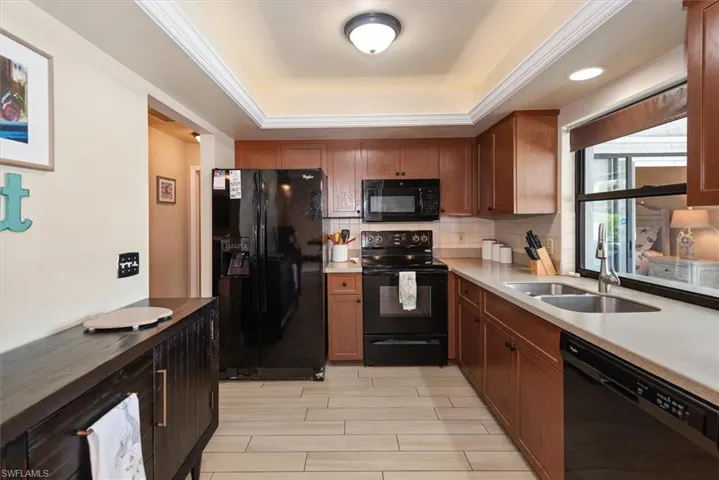 Kitchen featuring black appliances, a sink, a raised ceiling, tasteful backsplash, and brown cabinetry