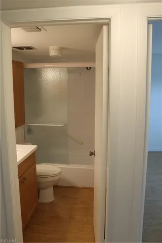 Bathroom with vanity, toilet, wood finished floors, and combined bath / shower with glass door