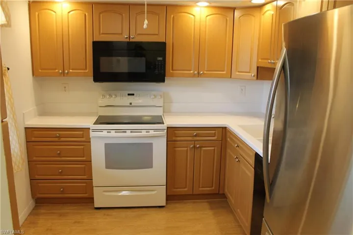 Kitchen featuring freestanding refrigerator, black microwave, white electric stove, light wood-type flooring, and light countertops