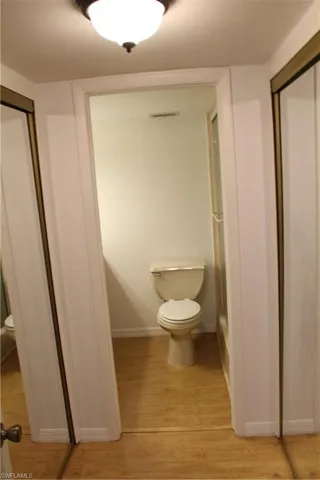 Bathroom featuring toilet, wood finished floors, and baseboards