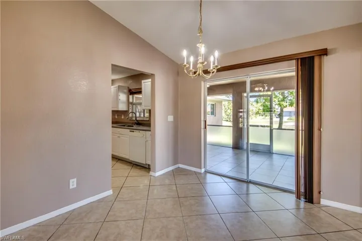 Unfurnished dining area featuring a sink, a chandelier, light tile patterned floors, vaulted ceiling, and baseboards