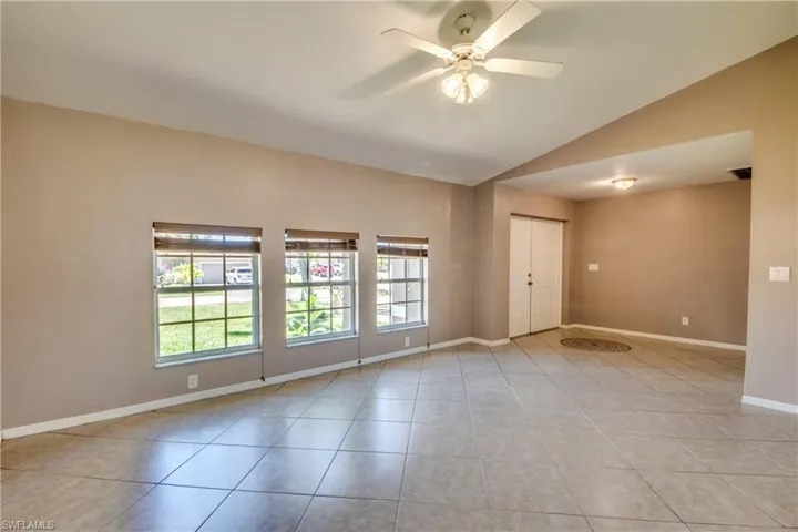 Empty room with vaulted ceiling, ceiling fan, light tile patterned flooring, and baseboards