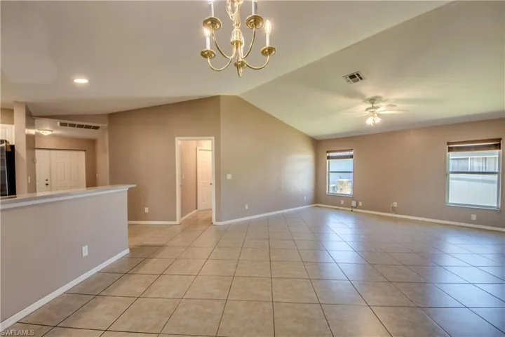 Unfurnished living room with light tile patterned floors, a ceiling fan, vaulted ceiling, baseboards, and a chandelier