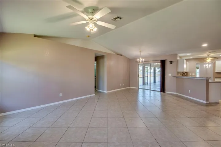 Unfurnished living room with ceiling fan, light tile patterned floors, a chandelier, lofted ceiling, and baseboards