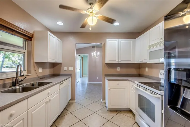 Kitchen with white appliances, a sink, light tile patterned flooring, white cabinets, and ceiling fan