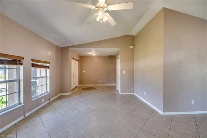 Empty room featuring vaulted ceiling, light tile patterned floors, a ceiling fan, and baseboards