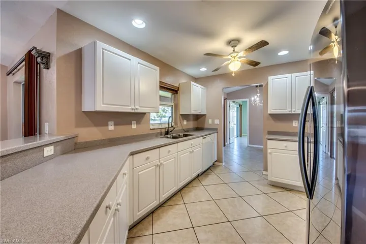 Kitchen featuring white dishwasher, refrigerator, a ceiling fan, a sink, and white cabinetry