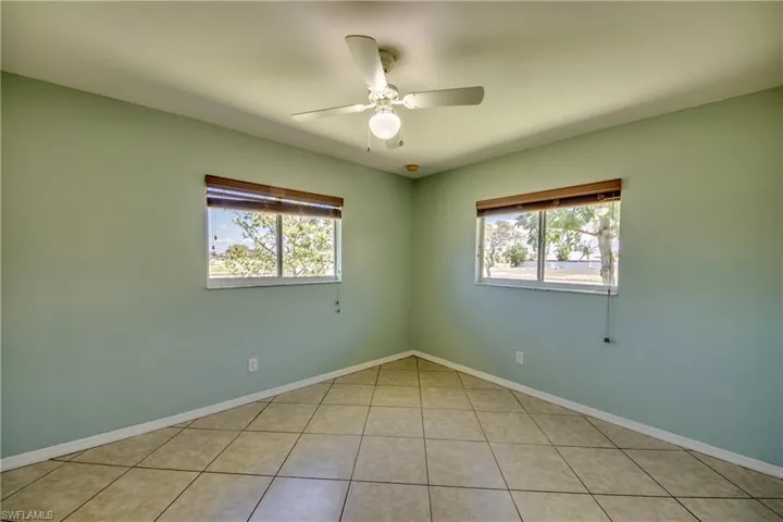 Empty room with plenty of natural light, a ceiling fan, light tile patterned floors, and baseboards