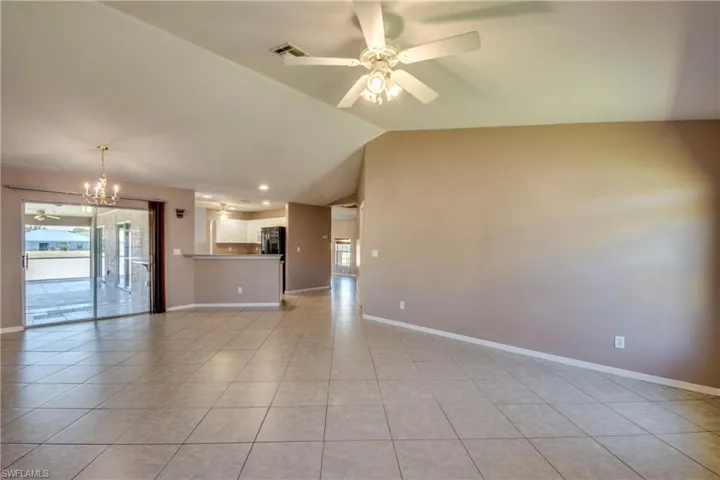 Unfurnished living room with healthy amount of natural light, vaulted ceiling, light tile patterned floors, a chandelier, and a ceiling fan