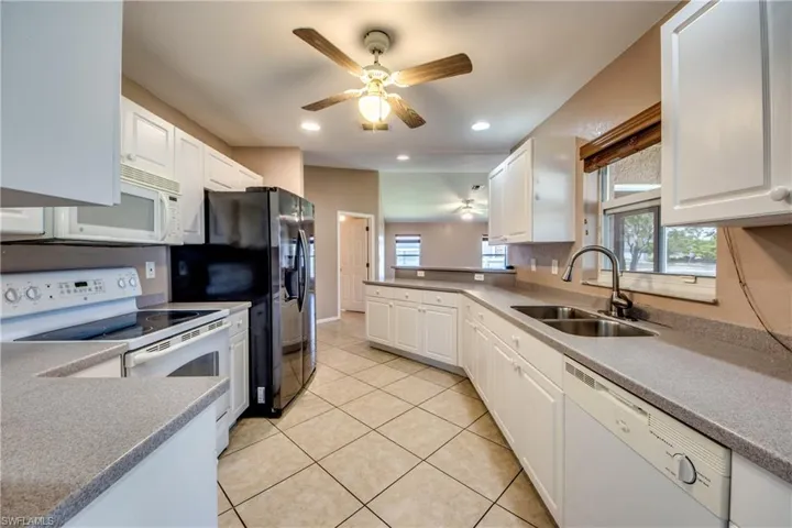 Kitchen featuring white appliances, a sink, ceiling fan, white cabinets, and light tile patterned floors