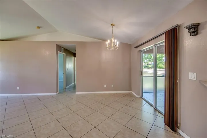 Unfurnished room featuring lofted ceiling, light tile patterned flooring, a chandelier, and baseboards