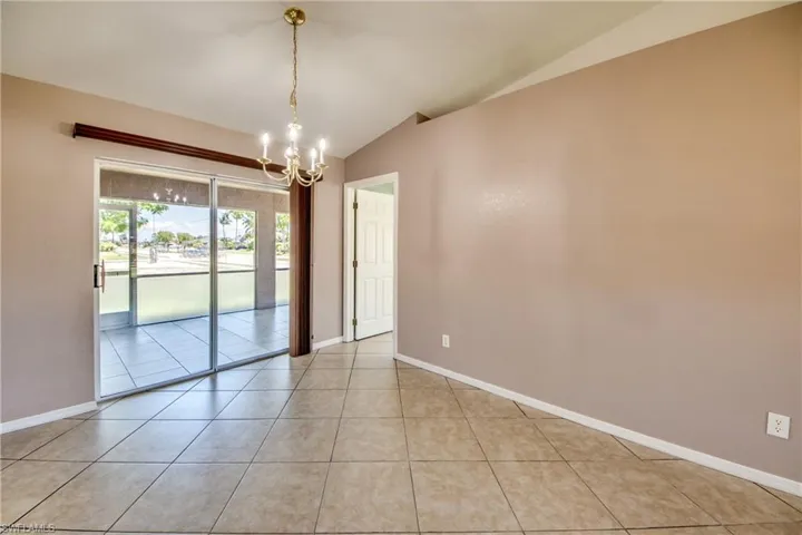 Empty room featuring lofted ceiling, a chandelier, light tile patterned floors, and baseboards
