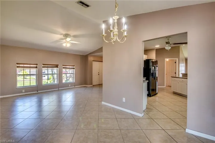 Unfurnished room with a ceiling fan, light tile patterned flooring, baseboards, lofted ceiling, and a chandelier