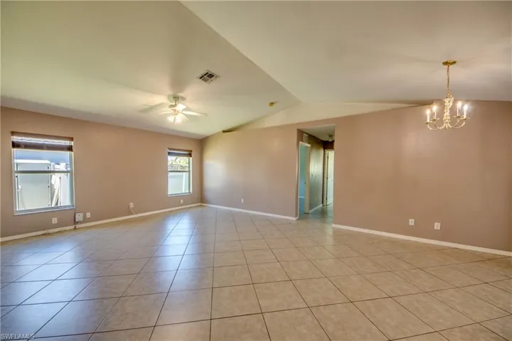 Empty room with vaulted ceiling, light tile patterned flooring, a ceiling fan, a chandelier, and baseboards
