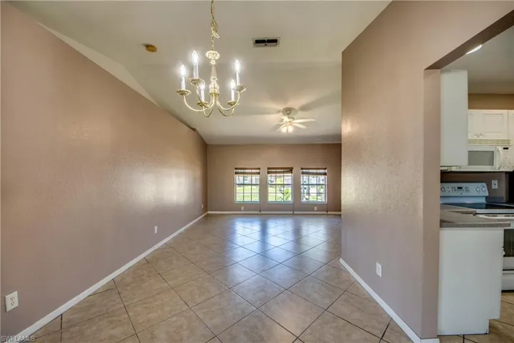 Unfurnished room featuring a ceiling fan, baseboards, a chandelier, and light tile patterned floors