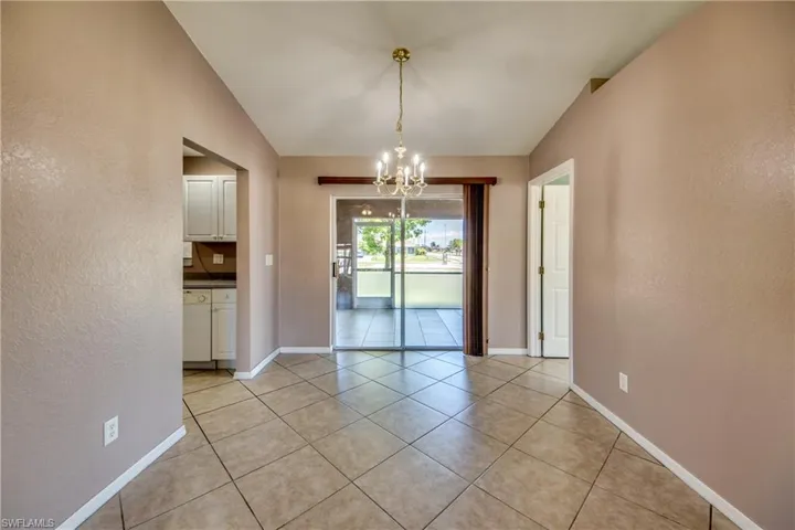Unfurnished dining area featuring a chandelier, light tile patterned floors, a textured wall, and baseboards
