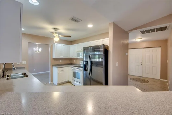 Kitchen featuring white appliances, a sink, ceiling fan, baseboards, and white cabinets