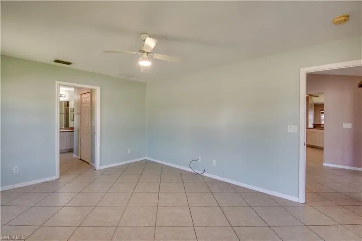 Empty room with a ceiling fan, light tile patterned floors, baseboards, and a smoke detector