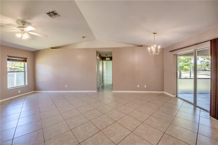 Spare room with a chandelier, light tile patterned floors, vaulted ceiling, baseboards, and ceiling fan