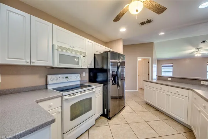 Kitchen with white appliances, ceiling fan, white cabinets, light tile patterned floors, and recessed lighting