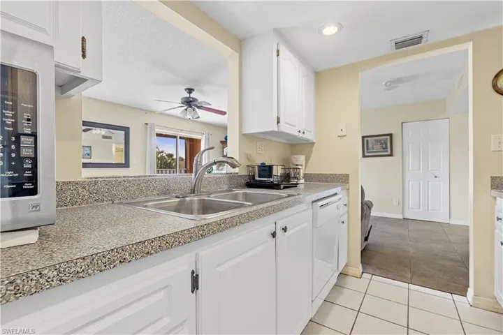 Kitchen with dishwasher, sink, light tile patterned flooring, white cabinets, and ceiling fan