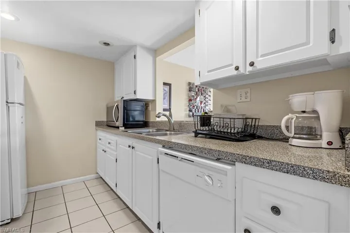 Kitchen with sink, white cabinets, white appliances, and light tile patterned floors