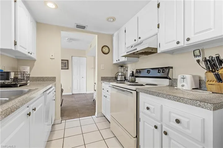 Kitchen featuring custom range hood, sink, light tile patterned flooring, white cabinetry, and white appliances