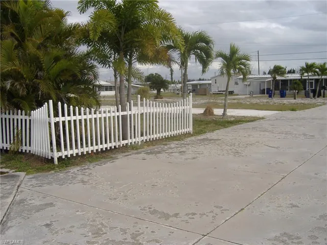The property features a white picket fence, mature palm trees, and a concrete driveway